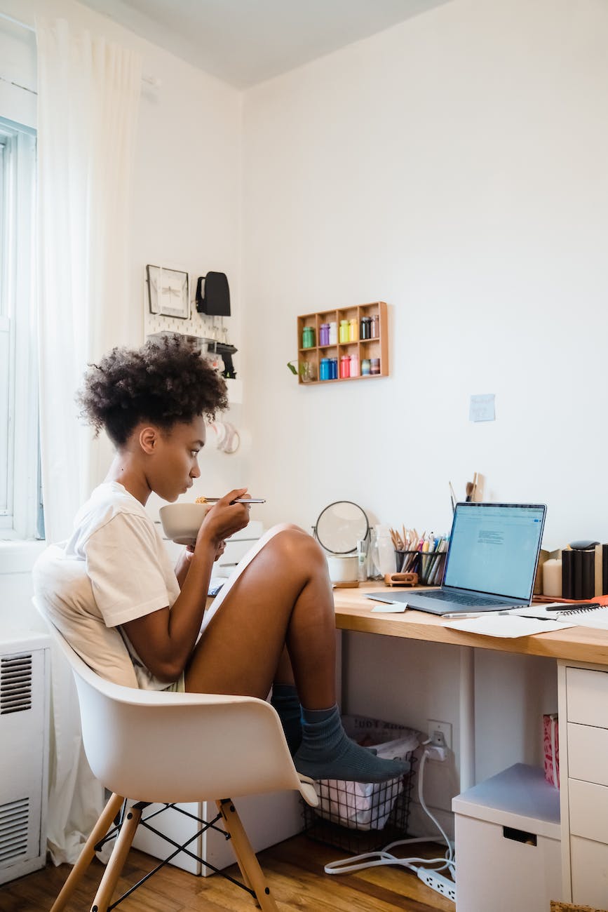 woman sitting behind a desk using laptop and eating food