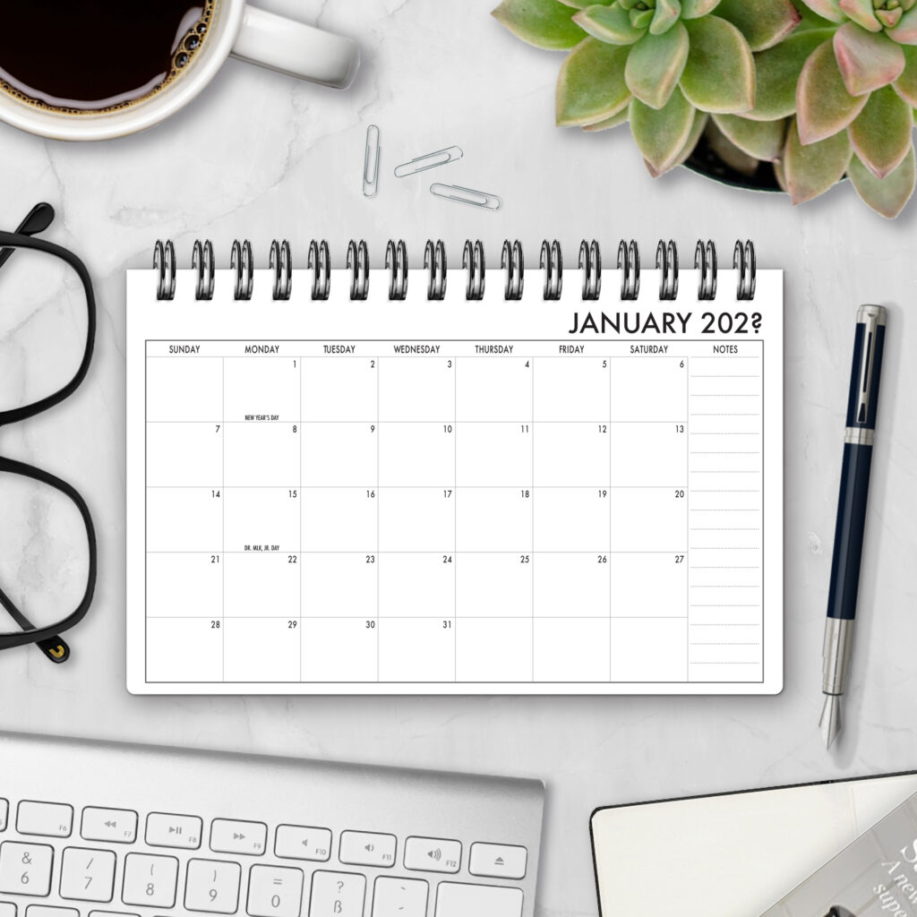 Top-bound landscape planner open to a January 2029 monthly calendar spread with Sunday-start grid and side notes column, styled on a marble desk with coffee, succulents, glasses, and a pen.