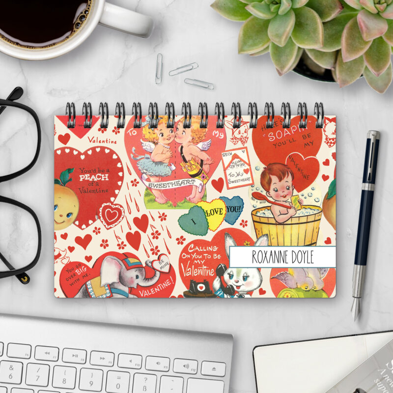 Top-bound landscape planner with an Sweetheart Flashback cover featuring a vintage collage of retro Valentine's Day cards — cherubs, hearts, an elephant, a rabbit, and sweet sayings — on a cream background, styled on a marble desk with coffee, succulents, glasses, and a pen.