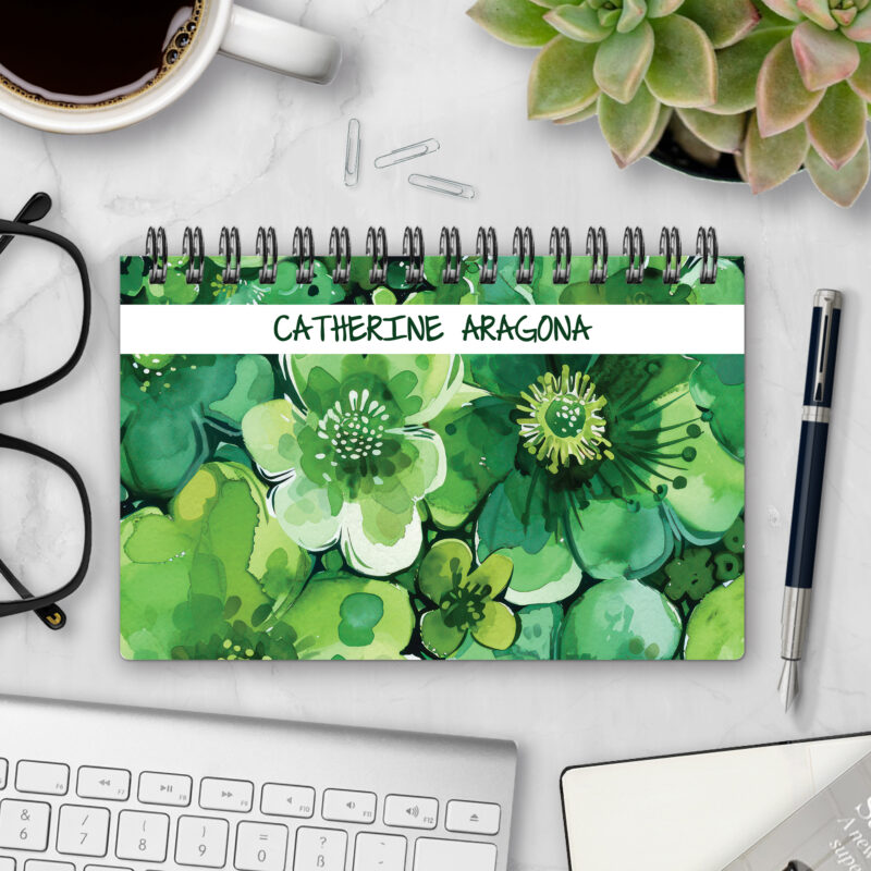 Top-bound landscape planner with a Verdant Blossoms cover featuring lush watercolor flowers in layered shades of green, styled on a marble desk with coffee, succulents, glasses, and a pen.