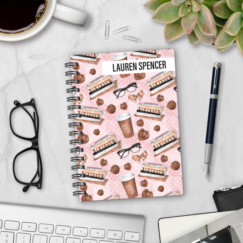 Personalized hardcover notebook in The Brew Review design with books, coffee cups, chocolates, and glasses on pink polka dot background styled with pen