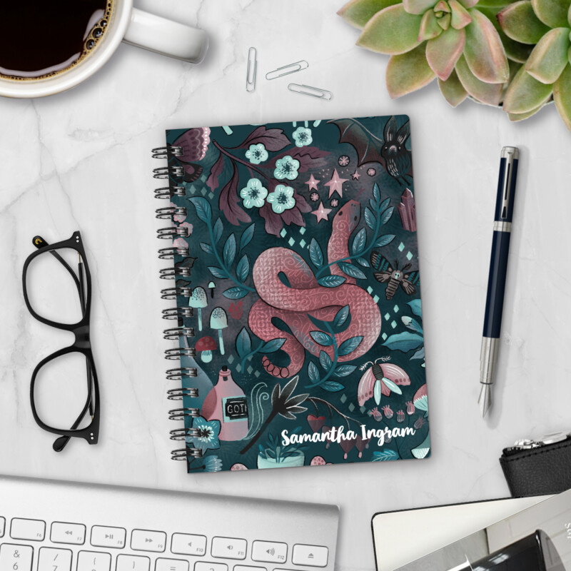 Personalized hardcover notebook in Into the Night design with pink snake, bat, moth, mushrooms, and goth florals on dark teal background styled with pen