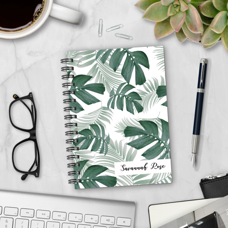 Personalized hardcover notebook in Botanical AF design with green monstera and palm leaves on white background styled on marble desk with coffee and pen
