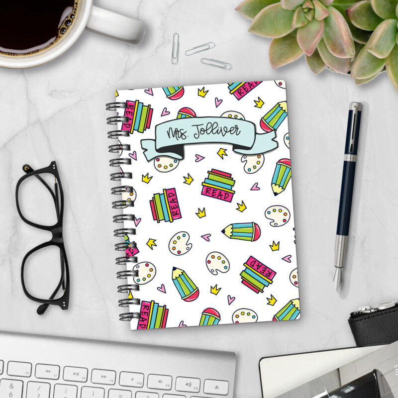 Personalized hardcover notebook in Grade Me Later design with colorful books, pencils, and paint palettes for teachers styled on marble desk with pen