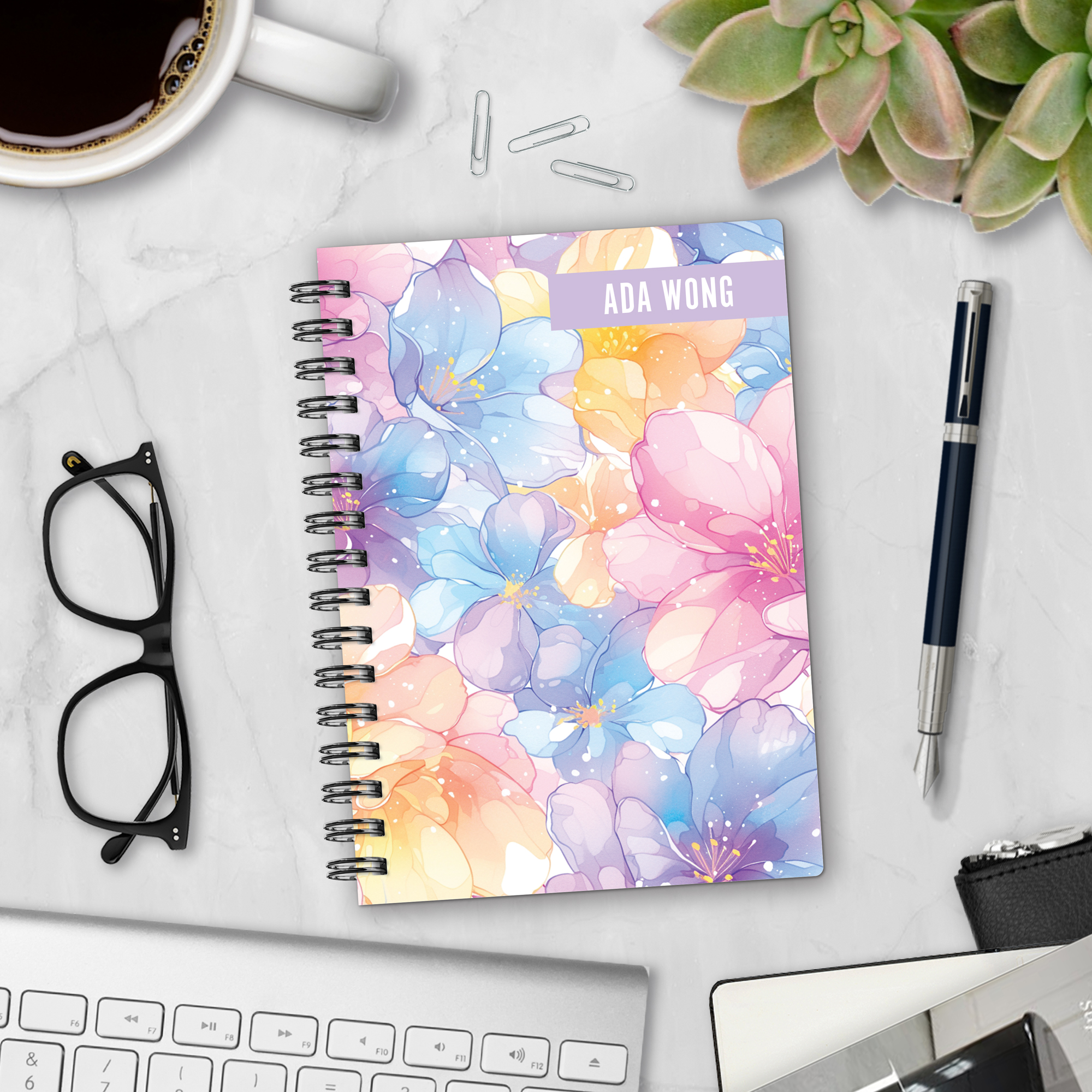 Personalized hardcover notebook in Spring Petals design with watercolor cherry blossoms and pastel flowers in pink, purple, blue, and yellow styled with pen