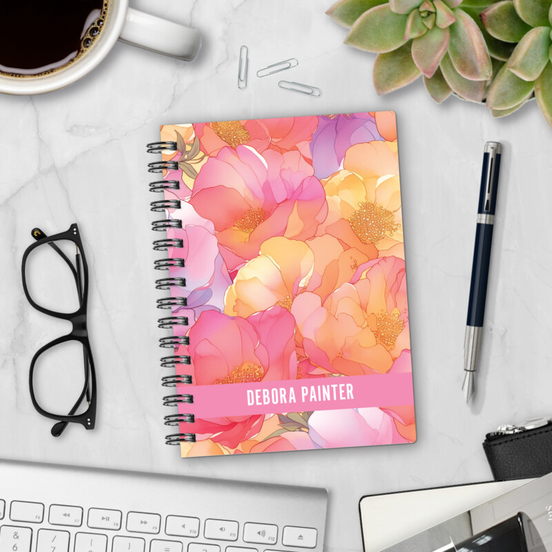 Personalized hardcover notebook in Sunset Blooms design with watercolor peonies in pink, coral, peach, and gold styled on marble desk with coffee and pen