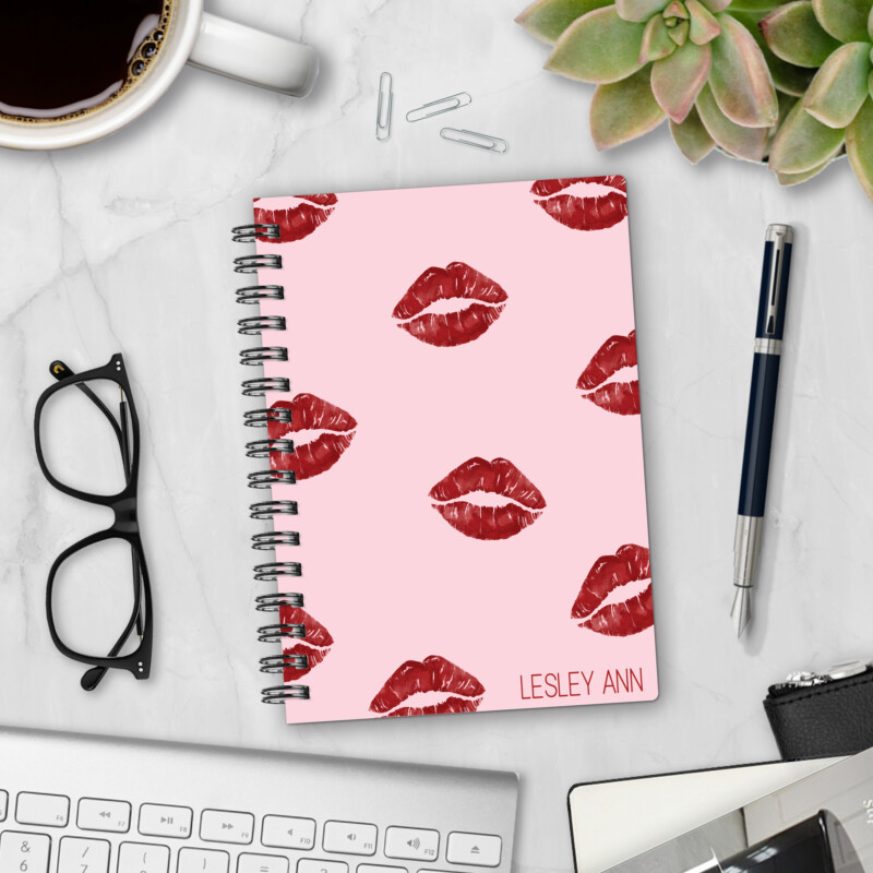 Personalized hardcover notebook in Hot Lips design with red lipstick kiss prints on pink background styled on marble desk with coffee, glasses, and pen
