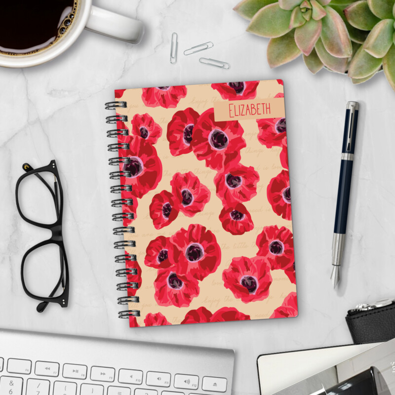 Personalized hardcover notebook in Poppy Prose design with red poppies and handwritten script on cream background styled on marble desk with coffee