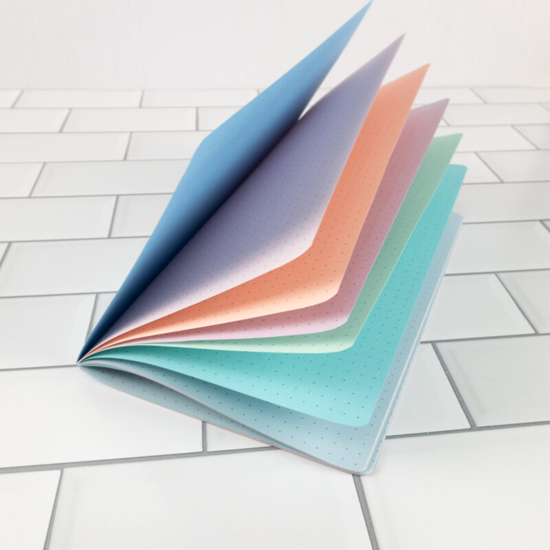 Cotton Candy traveler's notebook insert fanned open showing soft pastel pages in sky blue, lavender, peach, pink, mint, and teal.