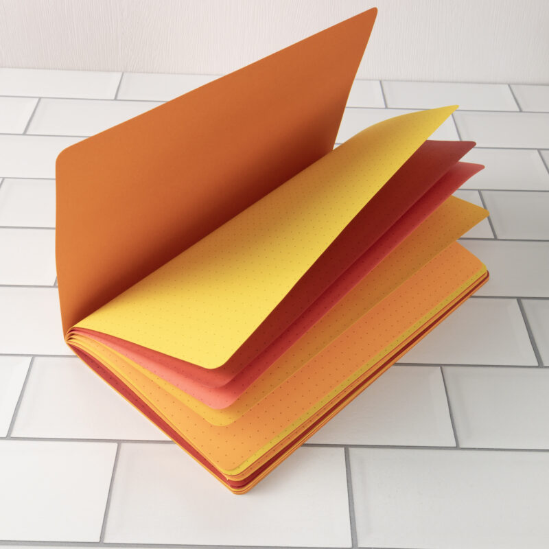 Dragon's Breath traveler's notebook insert fanned open showing fiery orange, yellow, red, and coral layered pages.