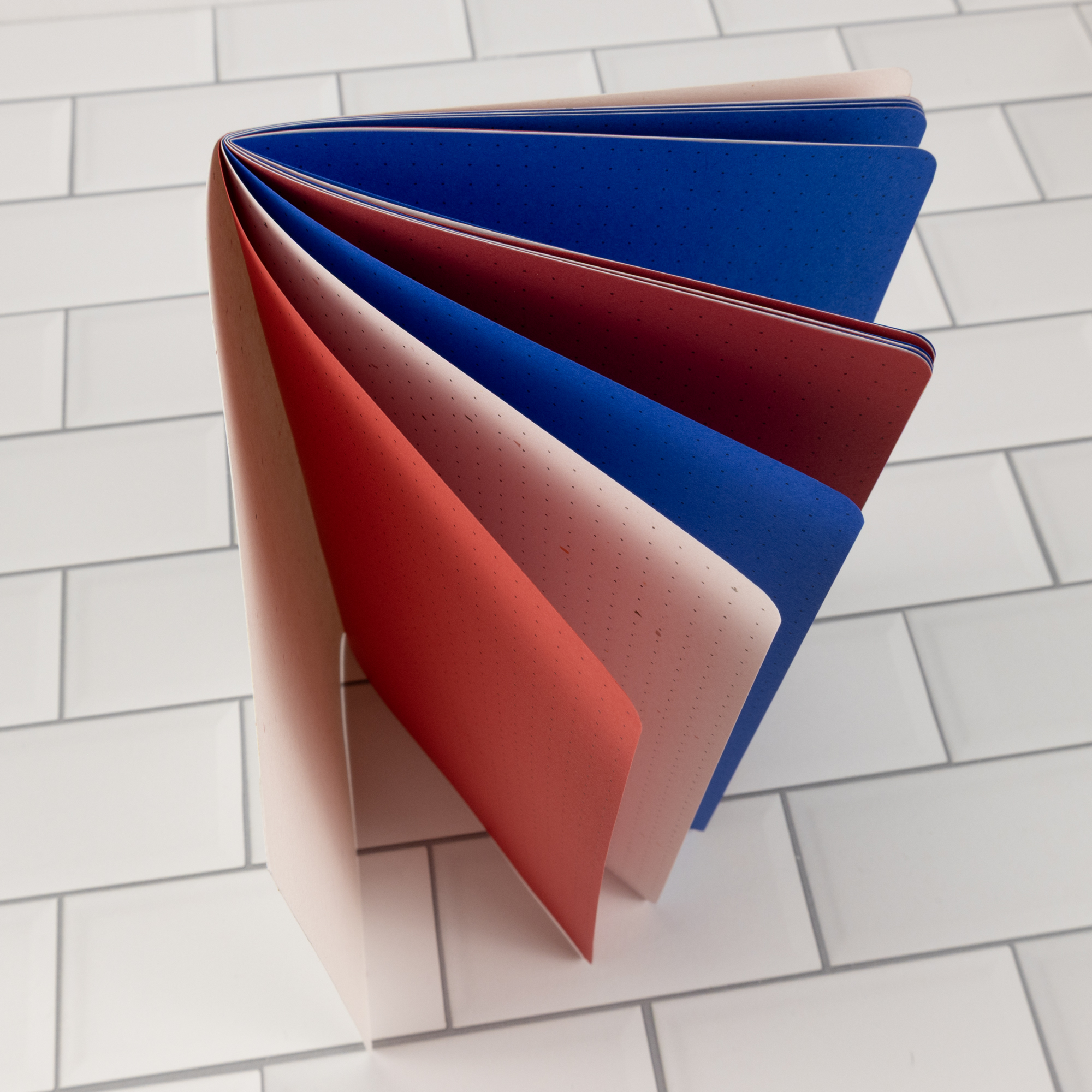 Firecracker traveler's notebook insert fanned open overhead showing patriotic red, speckled white, and blue pages.