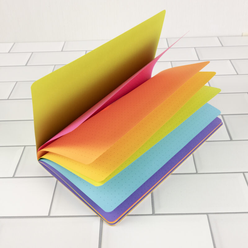 Piñata Party traveler's notebook insert fanned open showing bold rainbow pages in solar yellow, fuchsia, cosmic orange, terra green, lunar blue, and gravity grape.