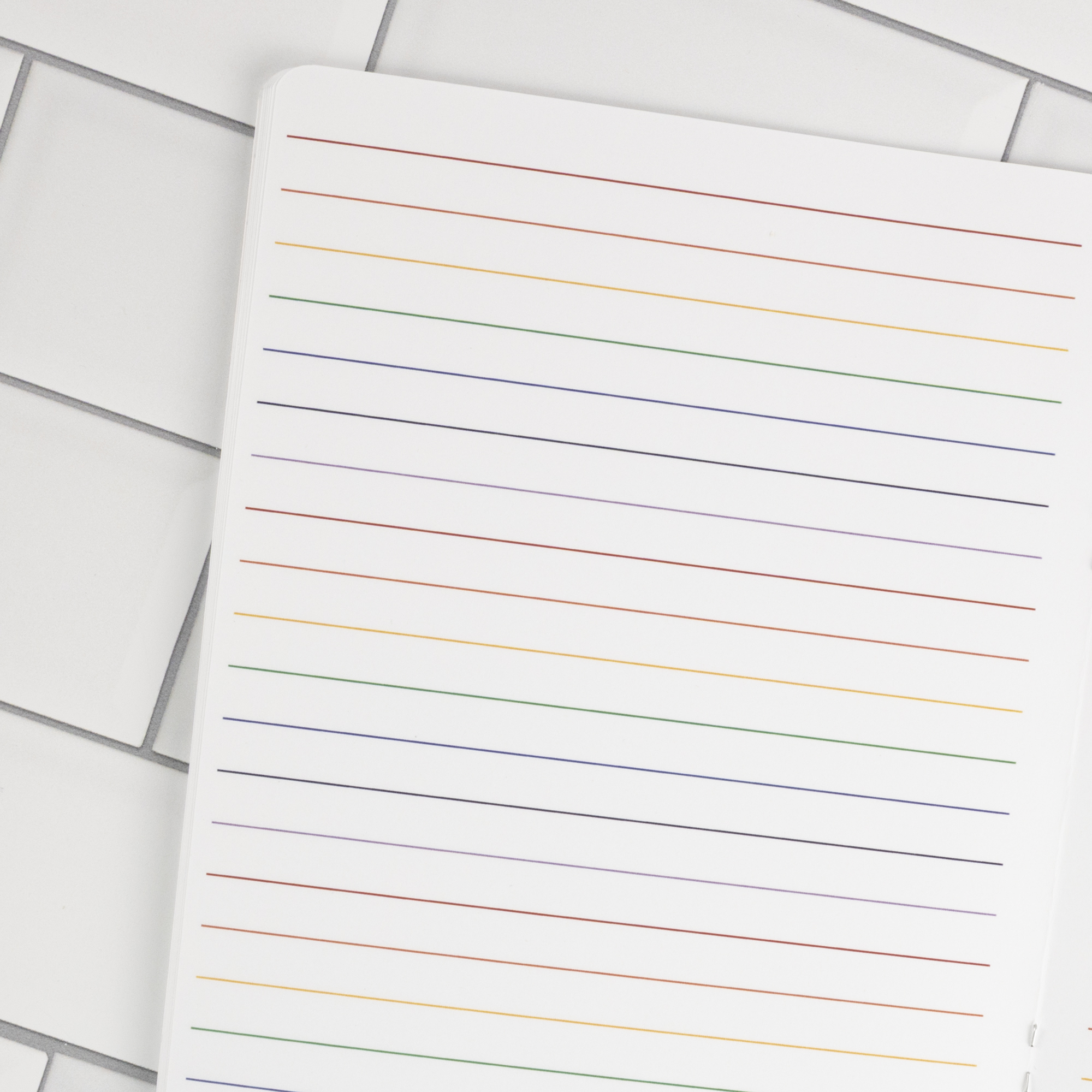 Prism traveler's notebook insert interior page detail showing white wide-ruled paper with ROYGBIV rainbow-colored lines.