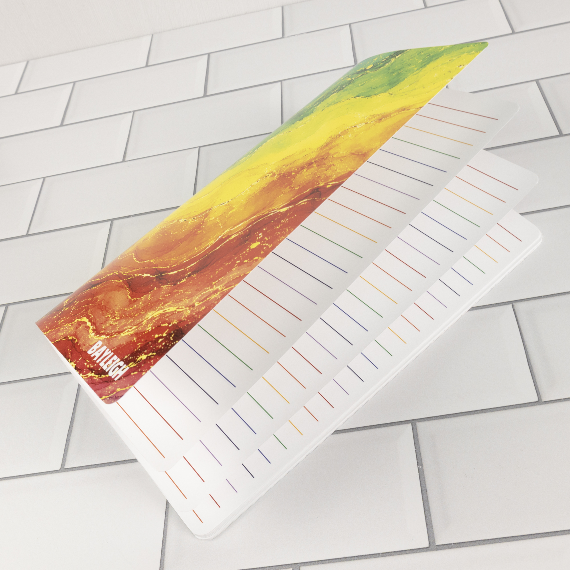 Prism personalized traveler's notebook insert open showing rainbow watercolor marble cover alongside white pages with rainbow-colored ruled lines.
