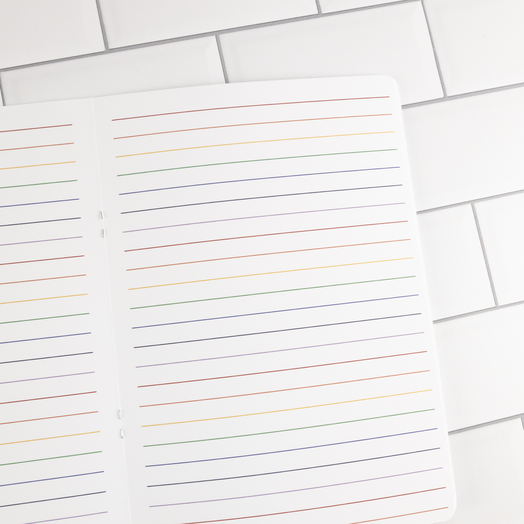 Prism traveler's notebook insert open flat showing two white pages with rainbow-colored ruled lines.