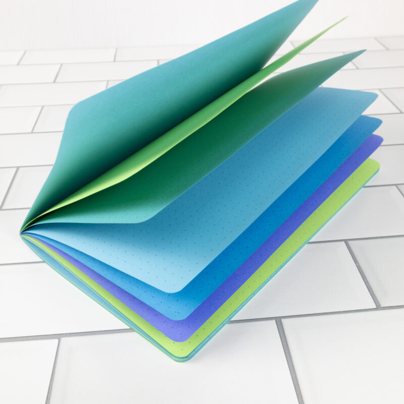 Mermaid Song traveler's notebook insert fanned open showing layered pages in teal, green, sky blue, ocean blue, and lavender.