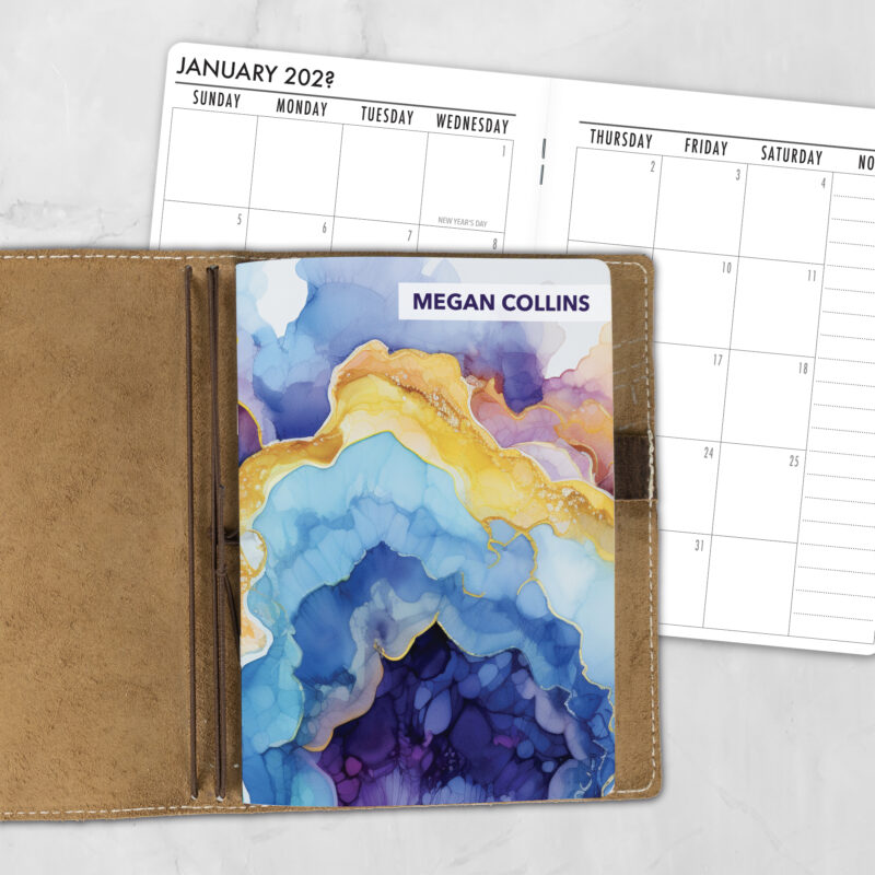 A5 Amethyst Geode personalized traveler's notebook refill showing the cover design inside a leather traveler's notebook cover, with a monthly calendar spread visible behind.