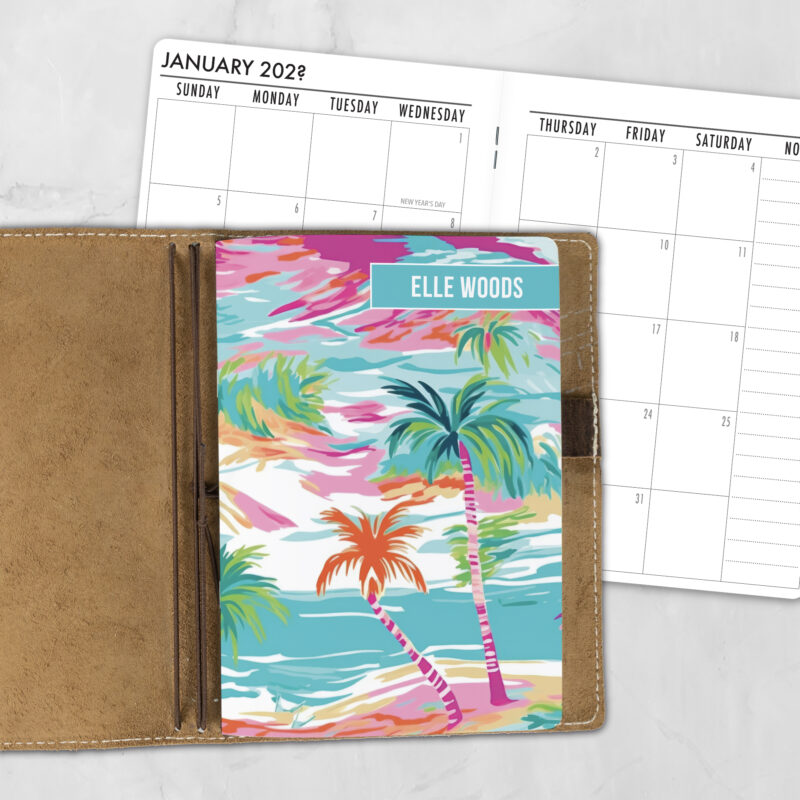 A5 Aquarelle Sky personalized traveler's notebook refill showing the cover design inside a leather traveler's notebook cover, with a monthly calendar spread visible behind.