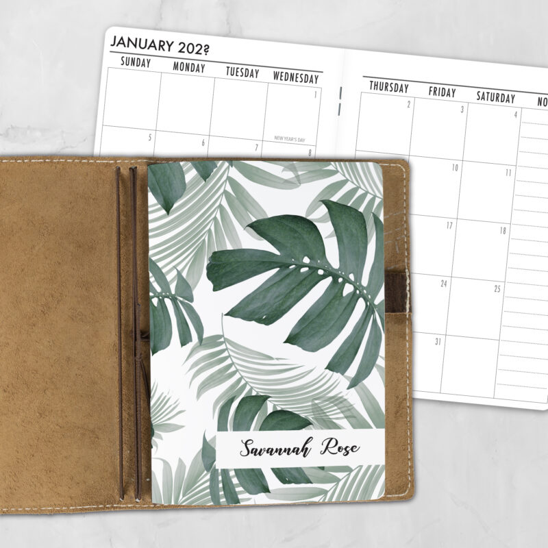 A5 Botanical AF personalized traveler's notebook refill showing the cover design inside a leather traveler's notebook cover, with a monthly calendar spread visible behind.