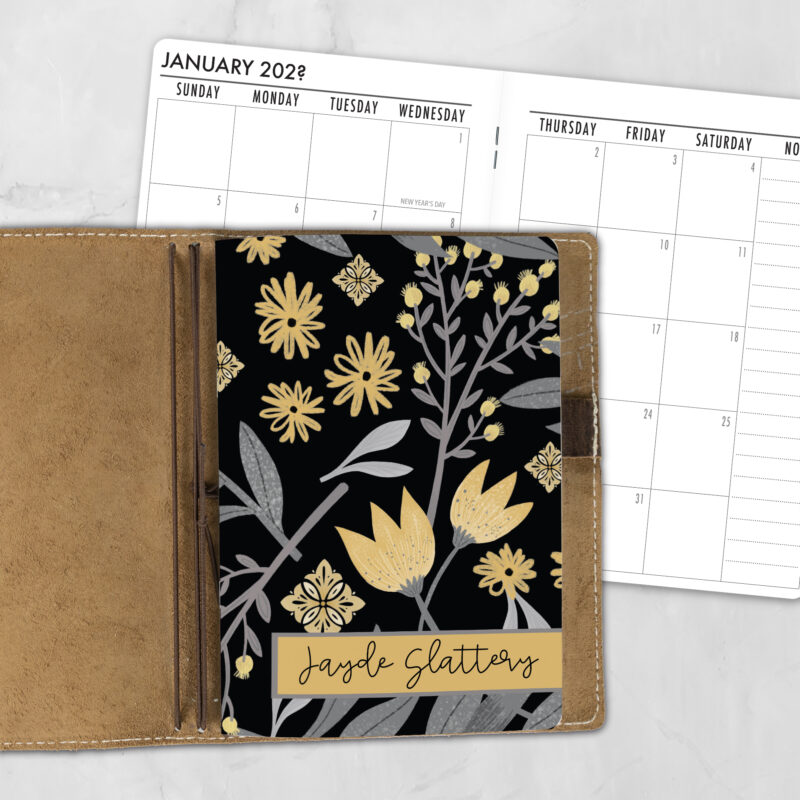 A5 Citrus Noir personalized traveler's notebook refill showing the cover design inside a leather traveler's notebook cover, with a monthly calendar spread visible behind.