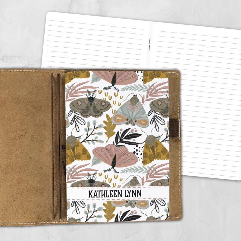 A5 Folkwing personalized traveler's notebook refill showing the cover design inside a leather traveler's notebook cover, with lined refill pages visible behind.