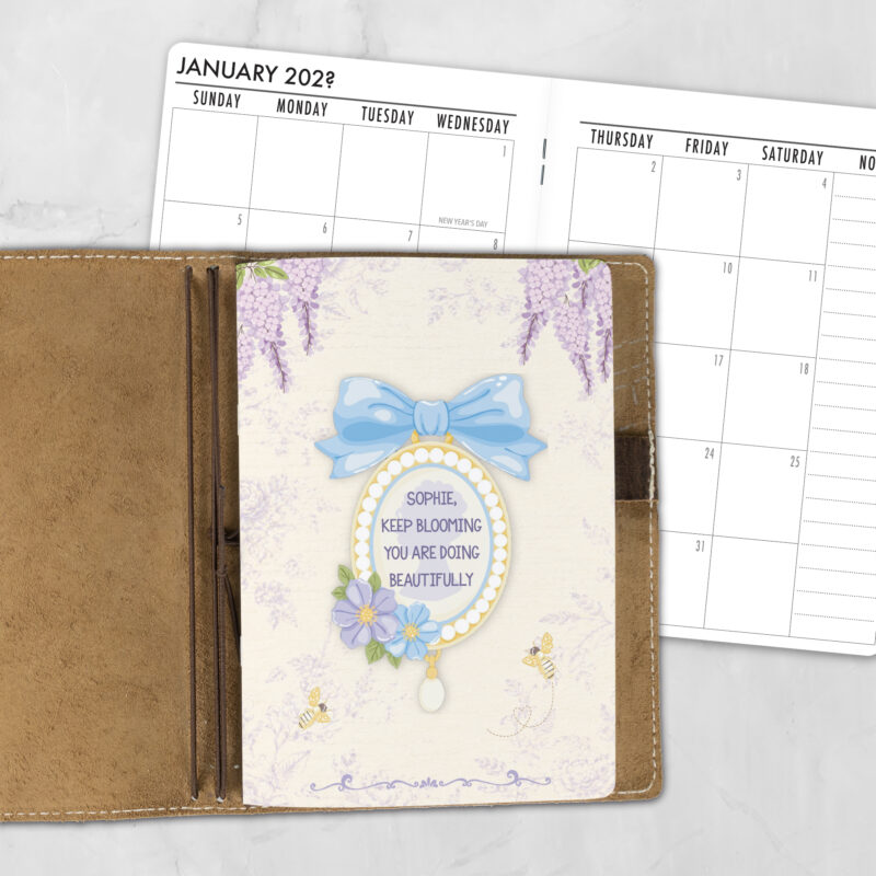 A5 Garden Tea personalized traveler's notebook refill showing the cover design inside a leather traveler's notebook cover, with a monthly calendar spread visible behind.