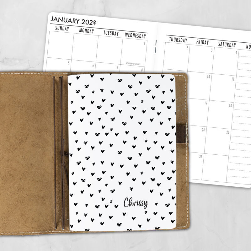 A5 Have a Heart personalized traveler's notebook refill showing the cover design inside a leather traveler's notebook cover, with a monthly calendar spread visible behind.