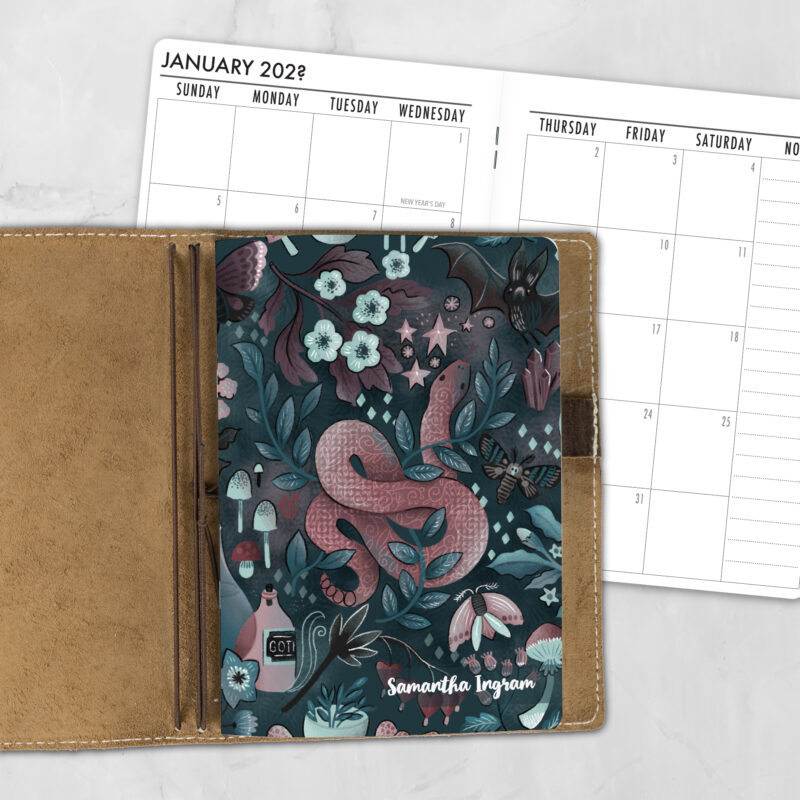 A5 Into the Night lifestyle personalized traveler's notebook refill showing the cover design inside a leather traveler's notebook cover, with a monthly calendar spread visible behind.