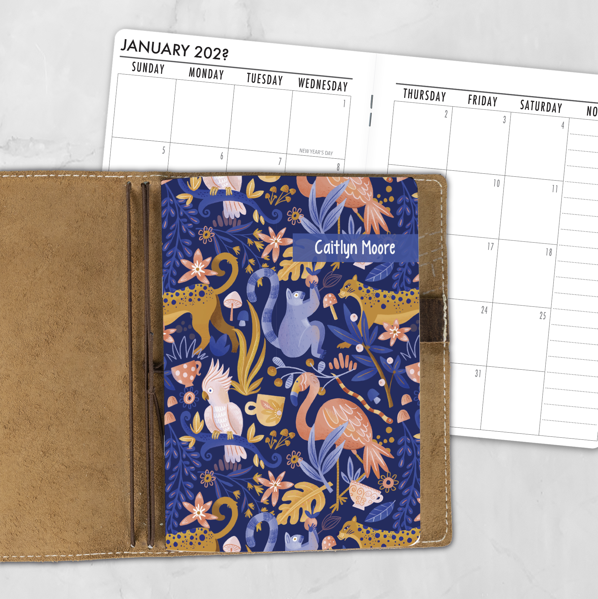 A5 Jungle Love lifestyle personalized traveler's notebook refill showing the cover design inside a leather traveler's notebook cover, with a monthly calendar spread visible behind.