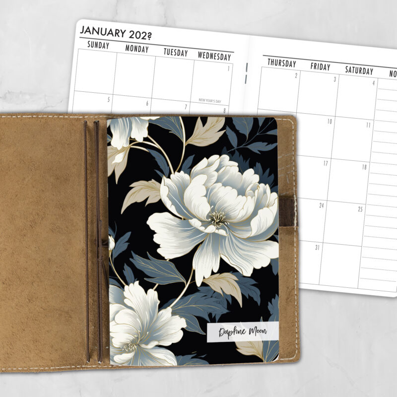 A5 Midnight Bloom Lifestyle personalized traveler's notebook refill showing the cover design inside a leather traveler's notebook cover, with a monthly calendar spread visible behind.