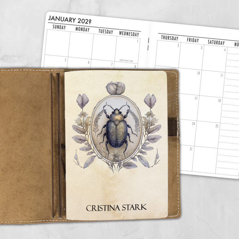 A5 Momento Insecta personalized traveler's notebook refill showing the cover design inside a leather traveler's notebook cover, with a monthly calendar spread visible behind.