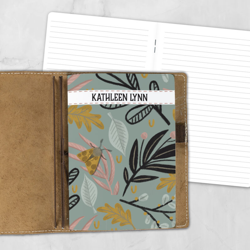 A5 Moth Fern personalized traveler's notebook refill showing the cover design inside a leather traveler's notebook cover, with lined refill pages visible behind.