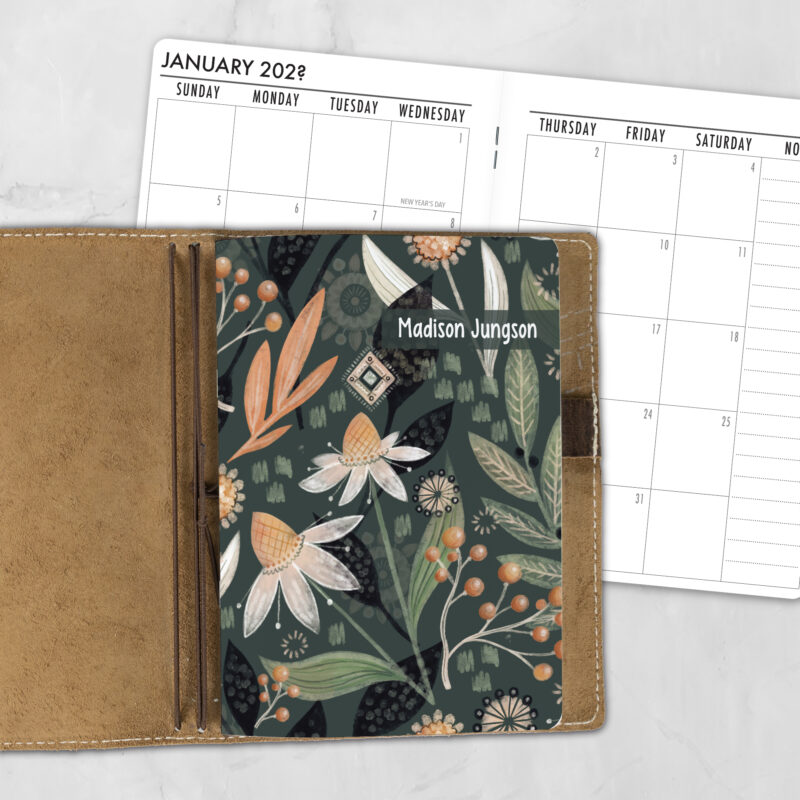 A5 Night Garden personalized traveler's notebook refill showing the cover design inside a leather traveler's notebook cover, with a monthly calendar spread visible behind.