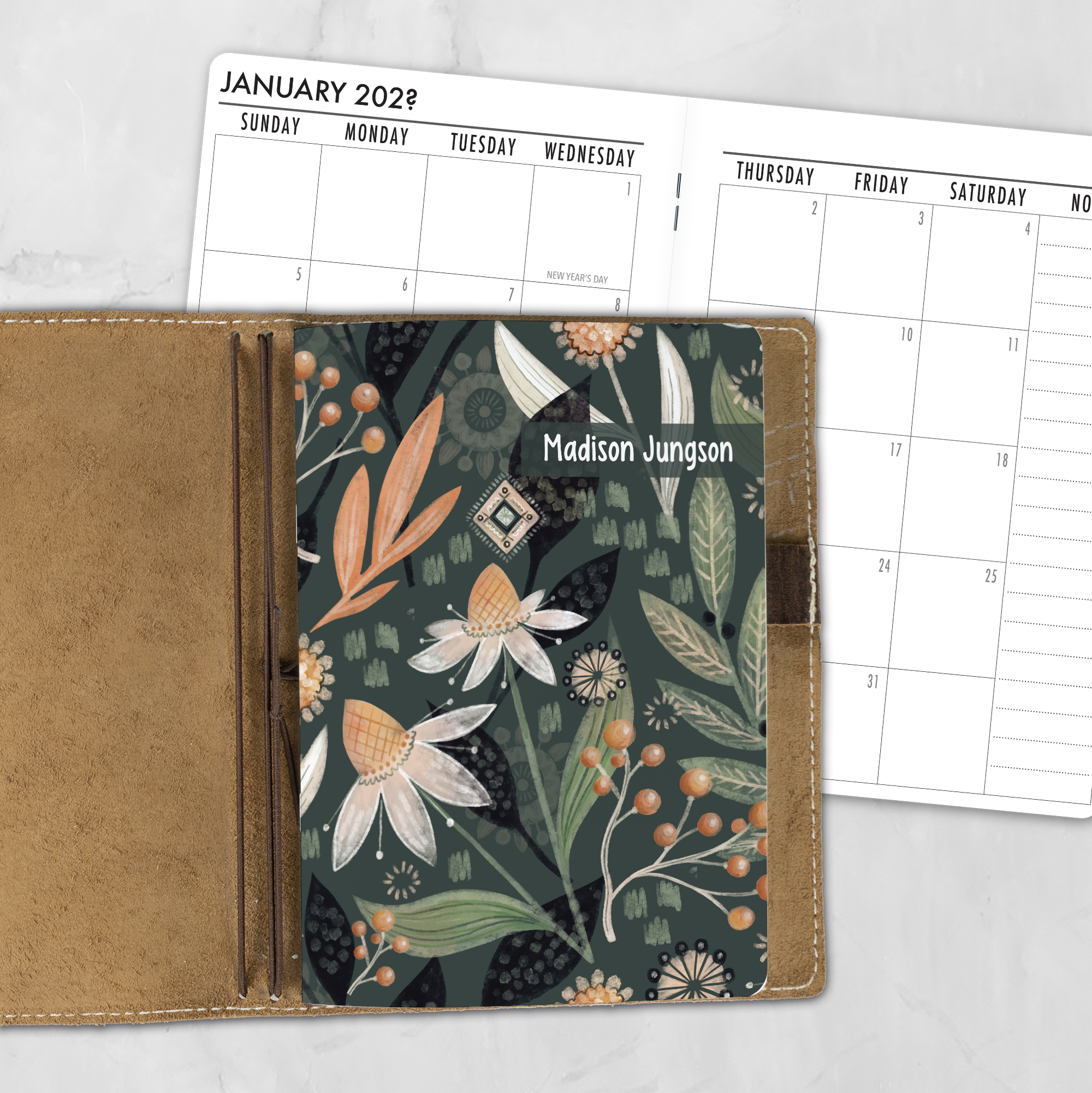 A5 Night Garden personalized traveler's notebook refill showing the cover design inside a leather traveler's notebook cover, with a monthly calendar spread visible behind.
