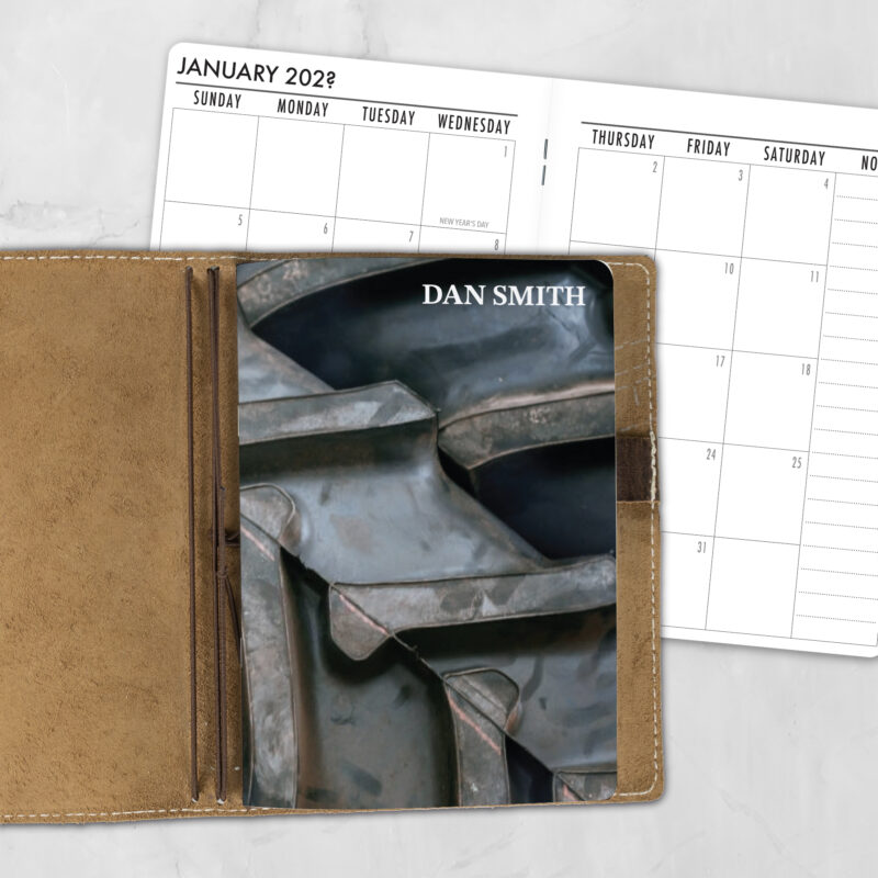 A5 Off Road Agenda Lifestyle personalized traveler's notebook refill showing the cover design inside a leather traveler's notebook cover, with a monthly calendar spread visible behind.