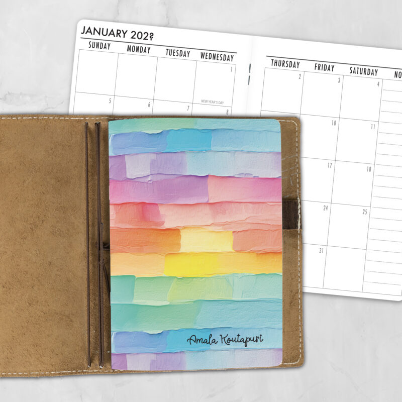 A5 Palette Cake personalized traveler's notebook refill showing the cover design inside a leather traveler's notebook cover, with a monthly calendar spread visible behind.