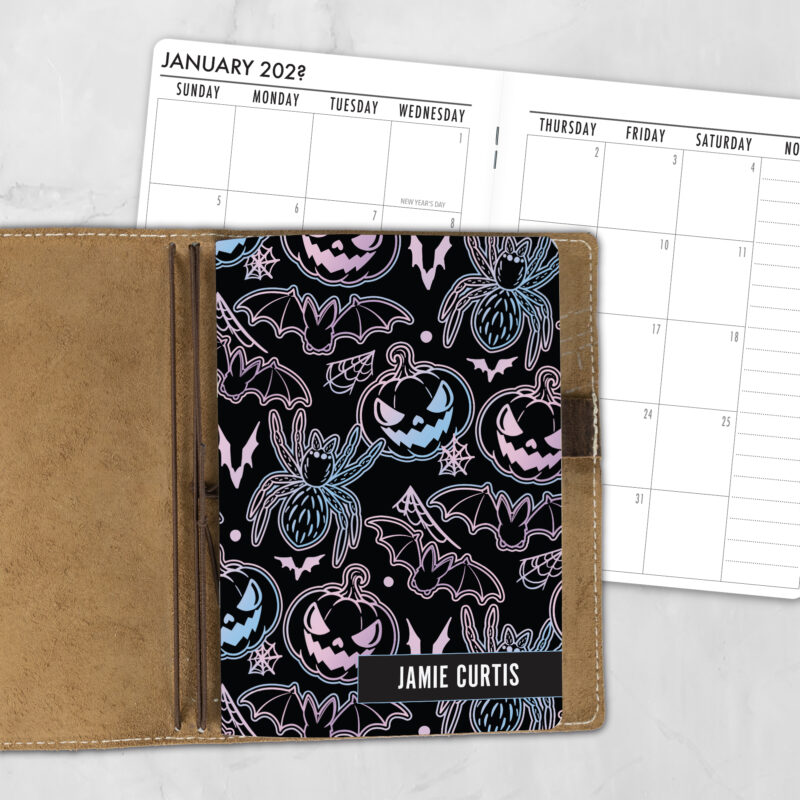 A5 Pastel Scream personalized traveler's notebook refill showing the cover design inside a leather traveler's notebook cover, with a monthly calendar spread visible behind.