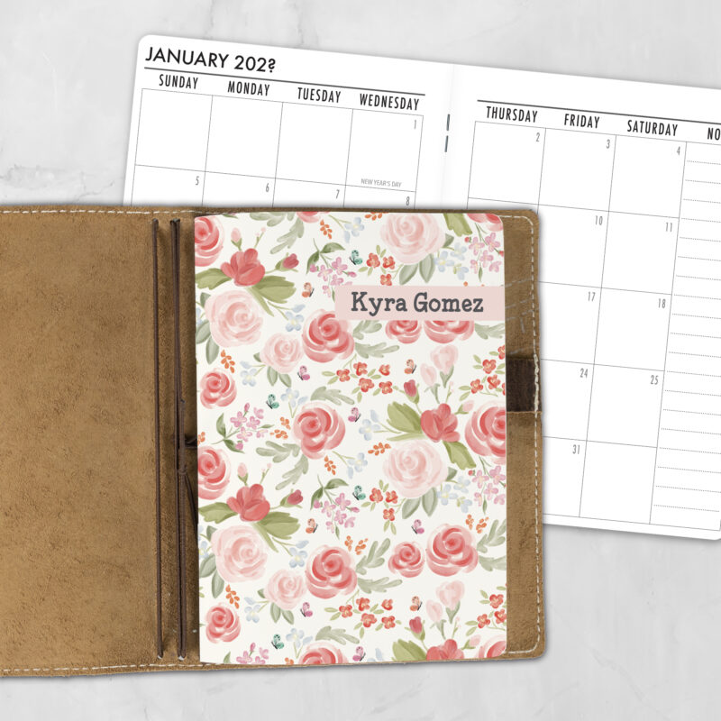 A5 Quiet Garden personalized traveler's notebook refill showing the cover design inside a leather traveler's notebook cover, with a monthly calendar spread visible behind.