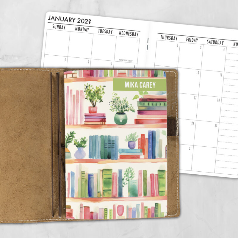 A5 Shelf Control personalized traveler's notebook refill showing the cover design inside a leather traveler's notebook cover, with a monthly calendar spread visible behind.