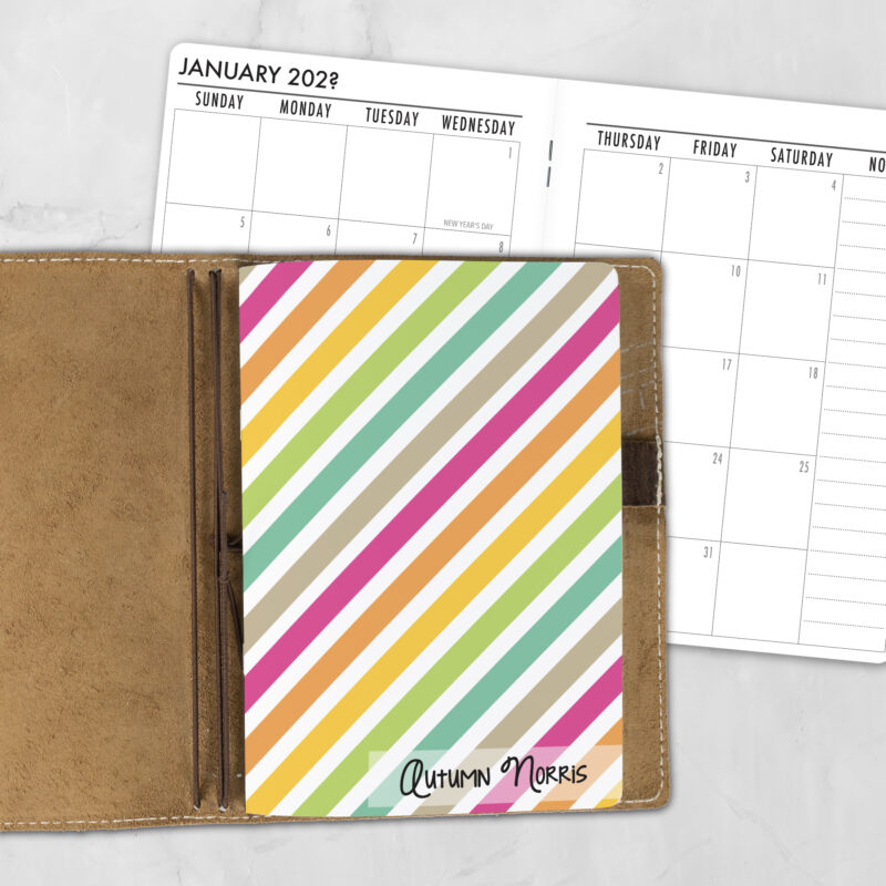 A5 Stripe Hype personalized traveler's notebook refill showing the cover design inside a leather traveler's notebook cover, with a monthly calendar spread visible behind.