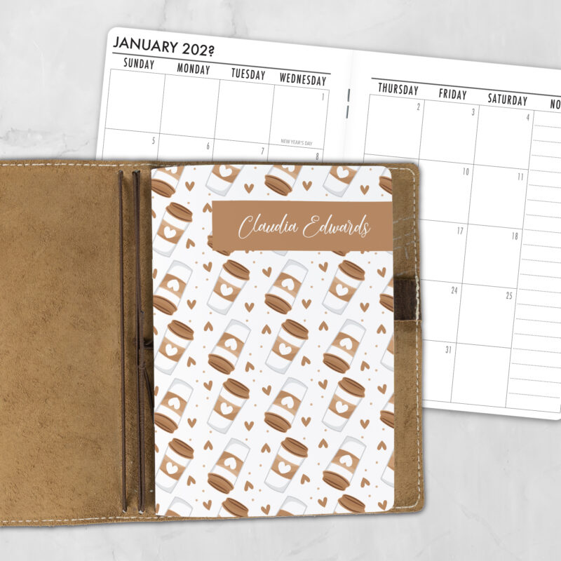 A5 Take a Sip personalized traveler's notebook refill showing the cover design inside a leather traveler's notebook cover, with a monthly calendar spread visible behind.