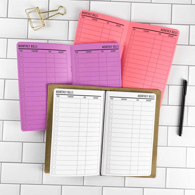Bill Tracker traveler's notebook refill by CityGirl Planners, showing bill tracking pages with columns for due dates, amounts, and payment status. Three booklets displayed in different paper color options inside a traveler's notebook cover.