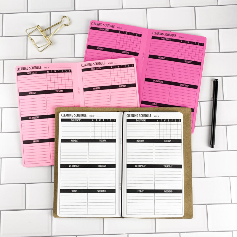 Cleaning Schedule traveler's notebook refill by CityGirl Planners, showing cleaning schedule tracker pages for organizing household tasks. Three booklets displayed in different paper color options inside a traveler's notebook cover.