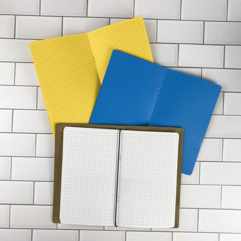 Cross Grid traveler's notebook refill by CityGirl Planners, showing cross grid pattern pages for note taking and sketching. Three booklets displayed in different paper color options inside a traveler's notebook cover.