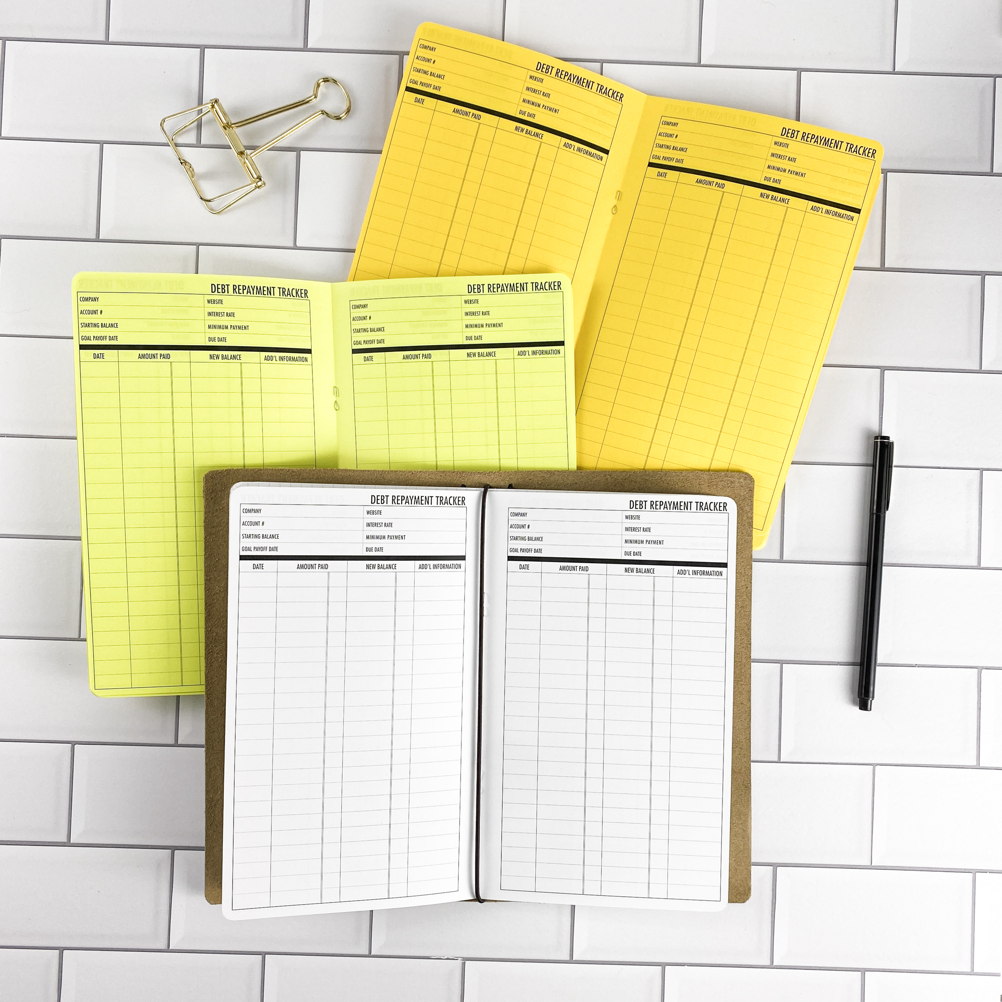 Debt Repayment traveler's notebook refill by CityGirl Planners, showing debt repayment tracker pages for managing payoff progress. Three booklets displayed in different paper color options inside a traveler's notebook cover.