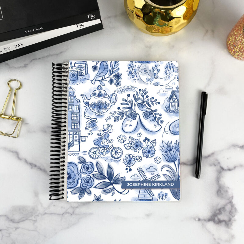 7x9 spiral bound planner in the Dutch Delft cover design on a marble surface with styling accessories.