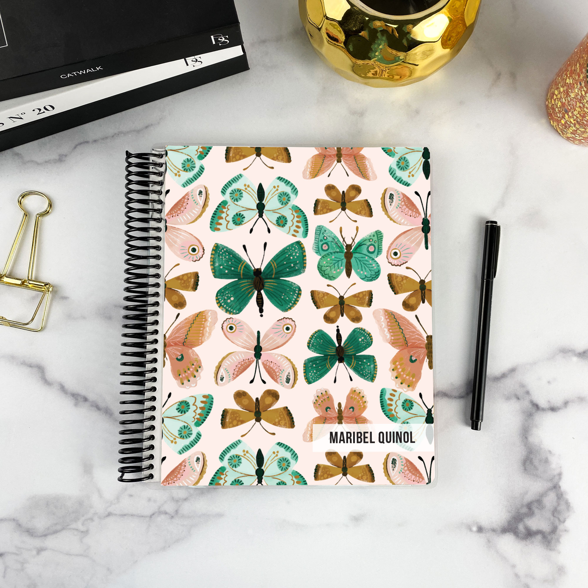 7x9 spiral bound planner in the Flutter By cover design on a marble surface with styling accessories.