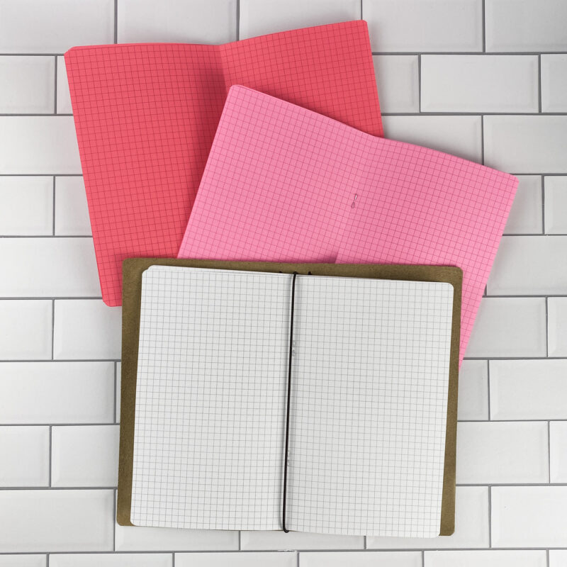 Graph Paper traveler's notebook refill by CityGirl Planners, showing graph paper grid pages. Three booklets displayed in different paper color options inside a traveler's notebook cover.