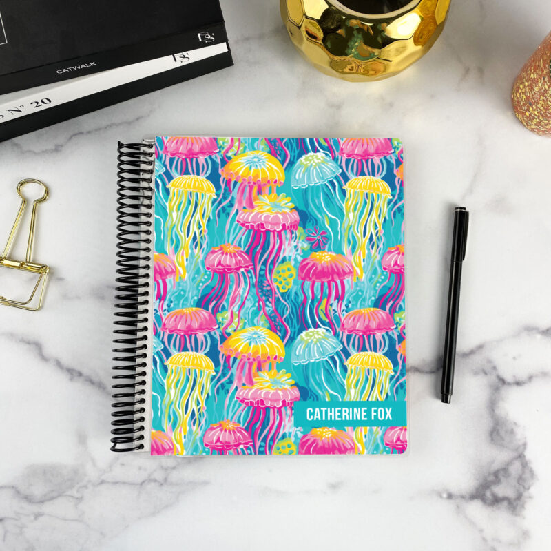7x9 spiral bound planner in the Neon jellyfish cover design on a marble surface with styling accessories.