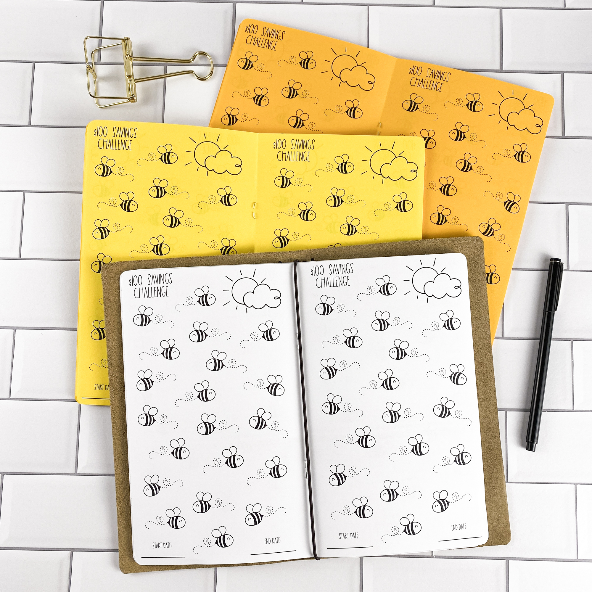 Savings Challenge Buzzin Bees traveler's notebook refill by CityGirl Planners, showing $100 savings challenge pages with cute bee illustrations to color in as you save. Three booklets displayed in different paper color options inside a traveler's notebook cover.